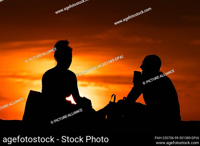 SYMBOL - 05 July 2023, Serbia, Belgrad: A woman and a man are sitting on a wall at Kalemegdan Park at sunset. Thereby they can be seen as a silhouette