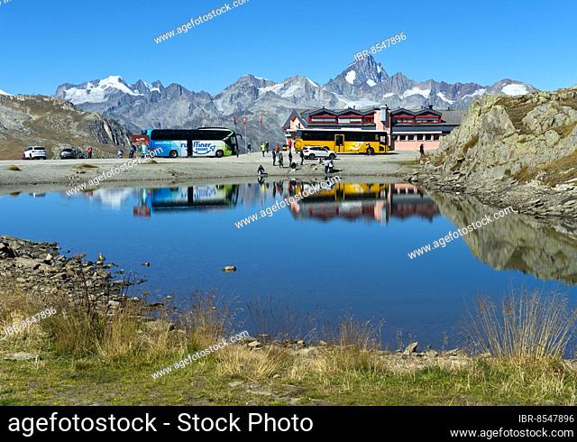 Coach with tourists and yellow bus of the Swiss PostBus AG on the Nufenen Pass, behind the mountain range of the Valais Alps with the Finsteraarhorn peak