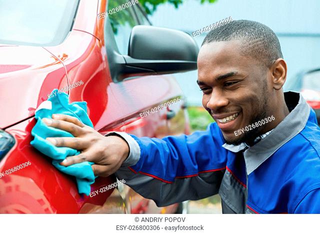 Young Happy Male Worker Cleaning Red Car With Cloth
