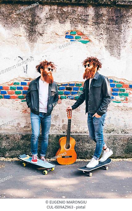 Young male hipster twins with red hair and beards on sidewalk with skateboards