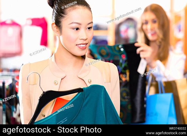 Asian and Caucasian Woman shopping in boutique or fashion store choosing clothes