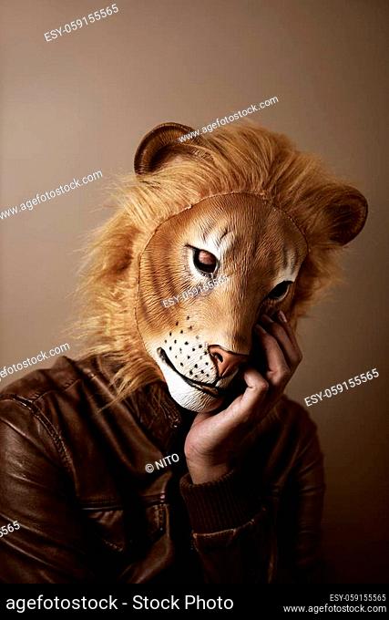 portrait of a man wearing a lion mask supporting his head in his hand, against a beige background, with a retro processing