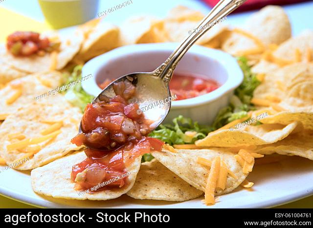 A close up view of a plate of nachos with salsa dip and a spoon