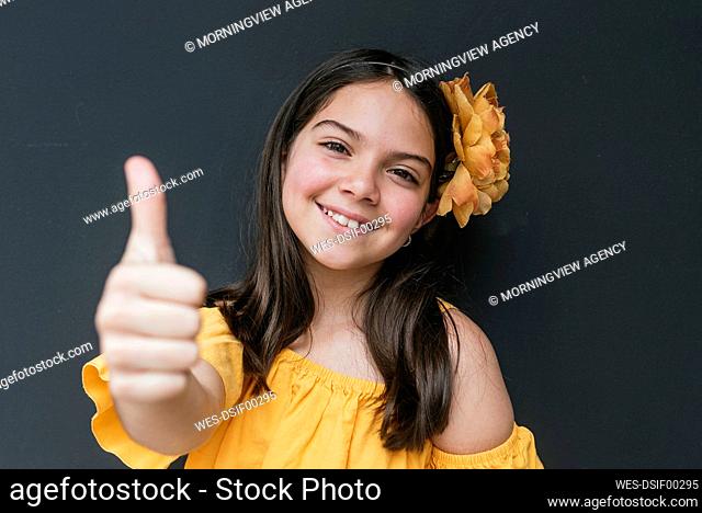 Close-up of smiling girl wearing yellow headband showing thumbs up against black background