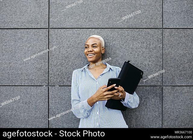 Smiling businesswoman with folder and phone against building in city