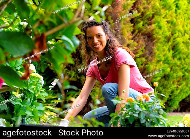 Portrait of smiling young biracial woman crouching while gardening in backyard