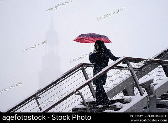 05 December 2023, Hamburg: A woman crosses a bridge in the snowy Speicherstadt district. The outline of Hamburg's Michel, the main church of St