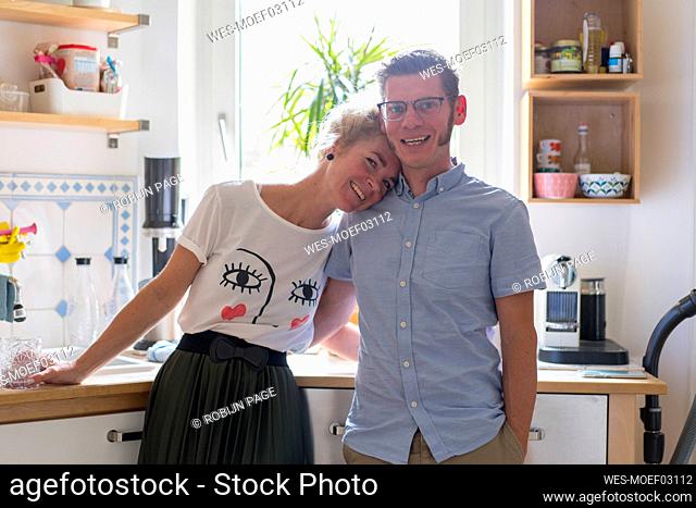 Smiling woman leaning on man's shoulder while standing in kitchen