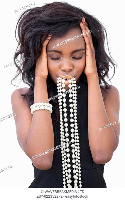 Woman standing with pearl necklace in her mouth against white background