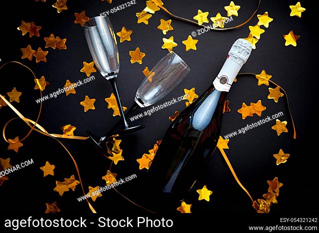 Glasses and bottle of champagne with golden serpentines and confetti lying on black background. New Year or party celebration concept. Top view