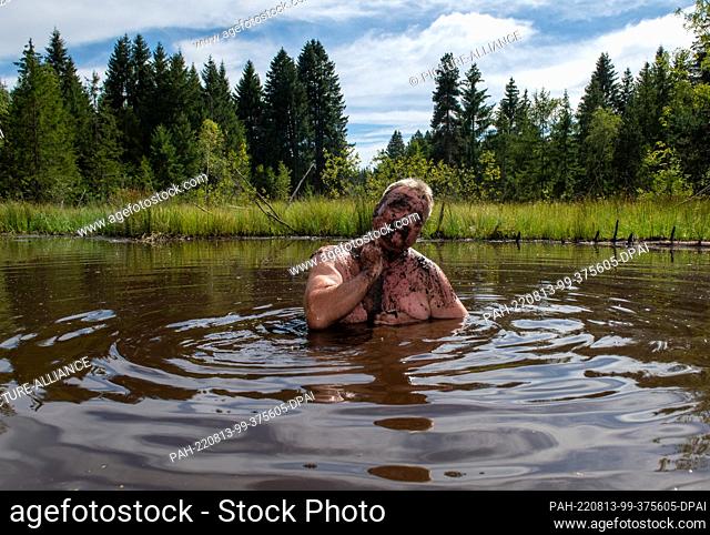 13 August 2022, Bavaria, Buchenberg: Achim Wurster bathes in a mud pond and rubs himself with mud. Thus, in addition to refreshment