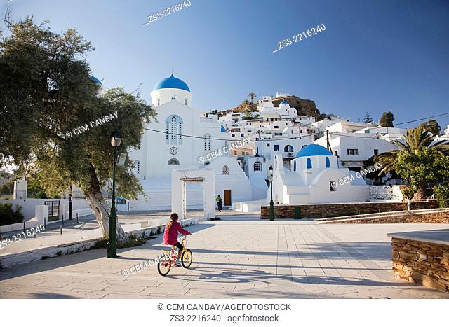 Girl riding a bike near a typical Cyclades church, a blue domed white Byzantine Greek Orthodox Chapel of Panaghia Gremiotissa in Chora, Ios, Cyclades Islands