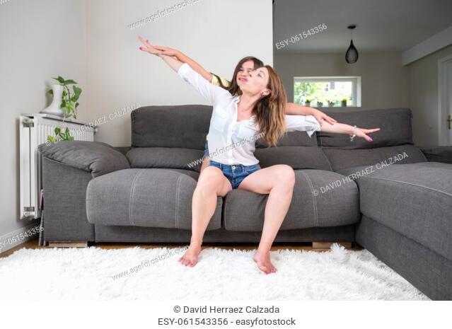 Playful and excited little girl holding her mother hands while pretending to fly for fun at home. Happy caucasian mother bonding and relaxing with her daughter