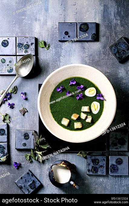 Nettle puree soup served with quail eggs, violet blossoms and croutons