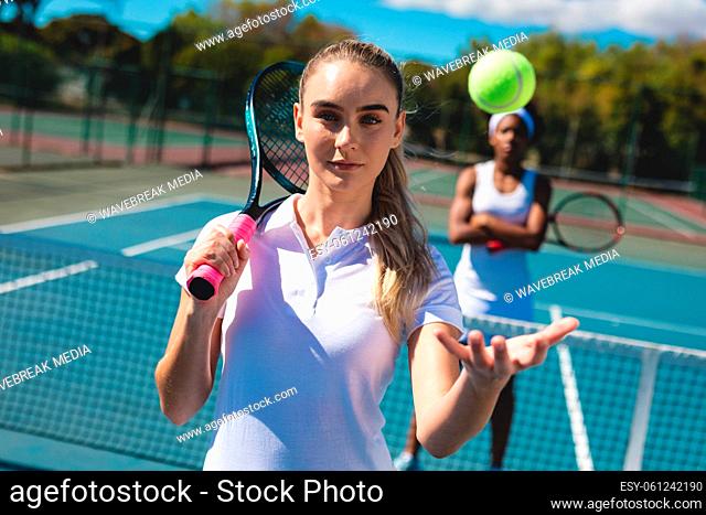Portrait of confident female caucasian tennis player catching ball with african american competitor