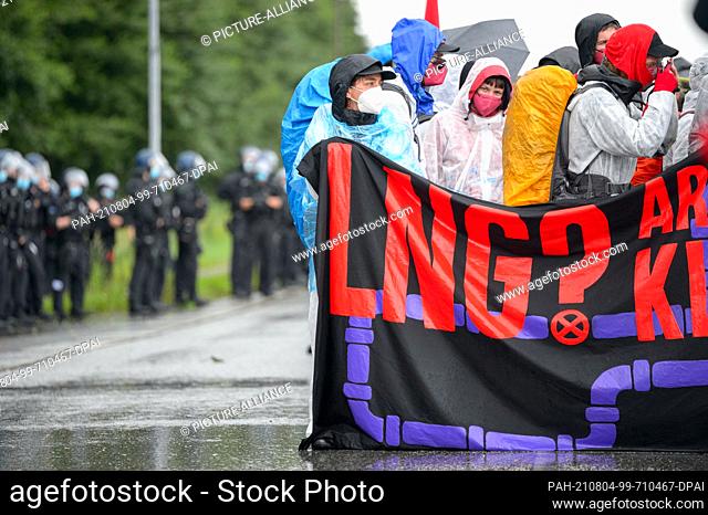 31 July 2021, Schleswig-Holstein, Brunsbüttel: Police officers stand next to a protest with a placard that reads ""LNG? Are you fracking kidding me?!"" at...