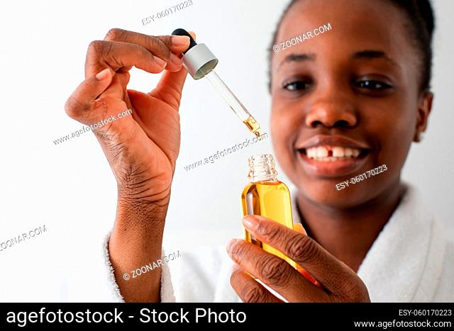 Beautiful black girl dropping argan oil into bottle holding pipette. Closeup african woman's hands with wrinkles holding bottle of argan oil and pipette