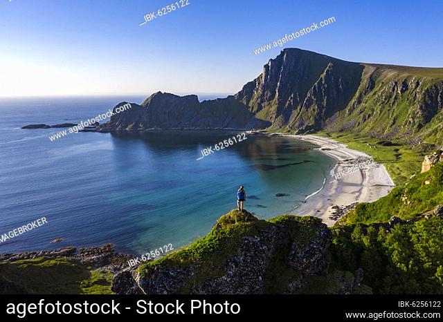 Hiker standing at the precipice, cliffs, beach and sea, in the back peak of the mountain Måtinden, near Stave, Nordland, Norway, Europe