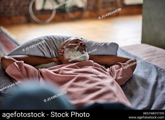 Mature man with hands behind head sleeping on bed at home