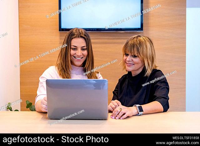 Smiling female dentist sitting by receptionist working on laptop at clinic