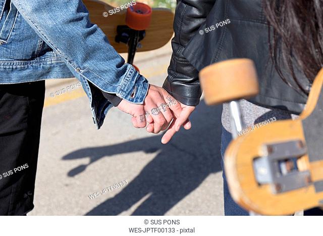 Tattooed young man holding hand with his girlfriend, partial view