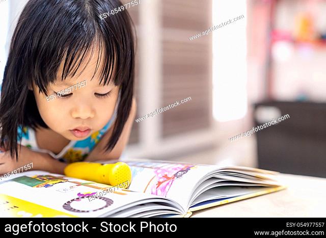 Asian girl child reading interactive book in living room at home as home schooling while city lockdown because of covid-19 pandemic across the world