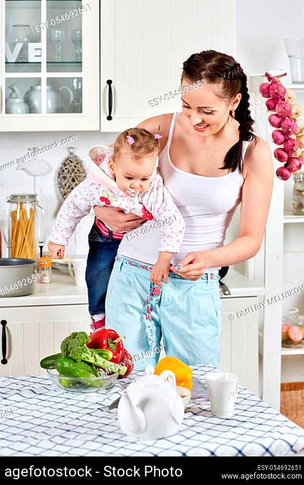 Young mother feeds little daughter in the home kitchen. Happy family
