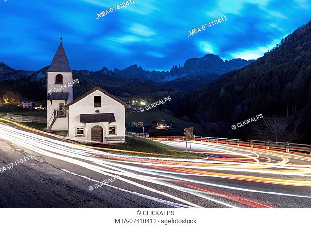 Lights of car trails around the Church of San Cipriano, Tires Valley, Dolomites, South Tyrol, Bolzano province, Italy