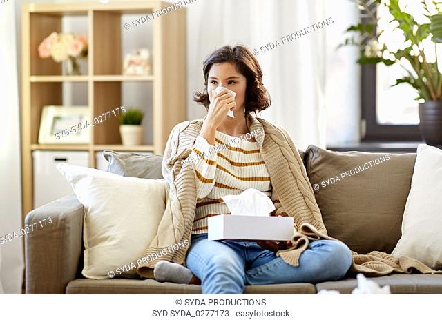 sick woman blowing nose in paper tissue at home