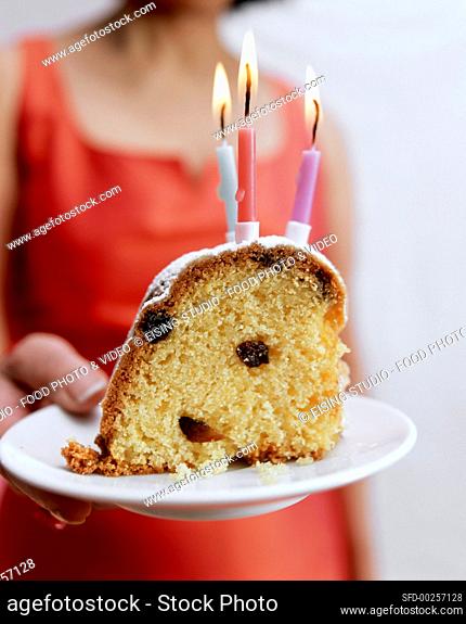 Woman serving piece of birthday gugelhupf with three candles