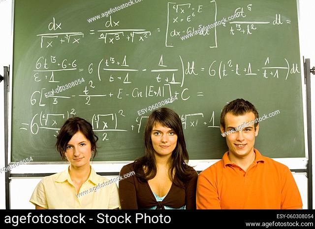 Small group of teenagers sitting in front of blackboard. Two girls and one boy. Looking at camera, front view