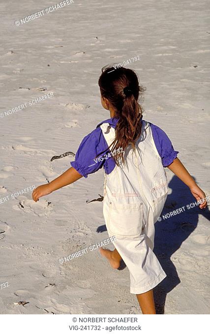 beach-scene, 6-year-old girl viewed from the back wearing white trousers with braces and a blue blouse walks bare feeted through the sand  - GERMANY, 26/06/2004