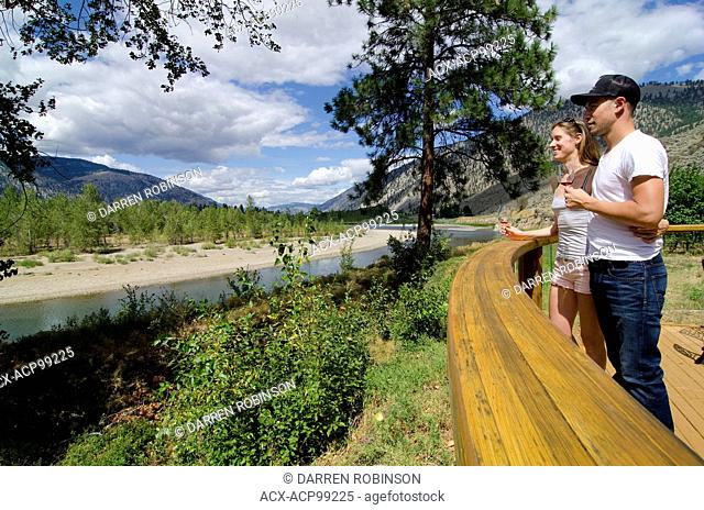 Young couple savours the view of the Similkameen River while sampling wine from Forbidden Fruit Winery, near Cawston, in the Similkameen region of British...