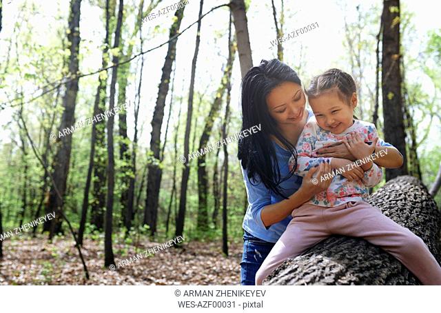Mother and daughter in park, sitting on tree trunk