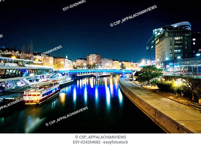 Modern buildings and boats along the Danube Canal at night, in Vienna, Austria