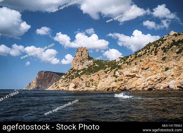 Tourist day trip pleasure boat moves along beautiful cliff landscape with white clouds in sky. Balaklava. Black sea Crimea