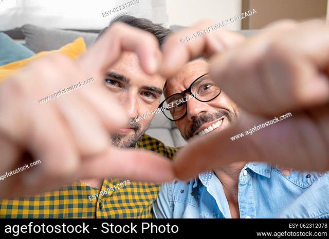 Young gay couple smiling confident doing heart symbol with hands at home. High quality photography