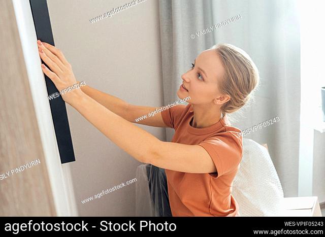 Young woman hanging frame in new apartment