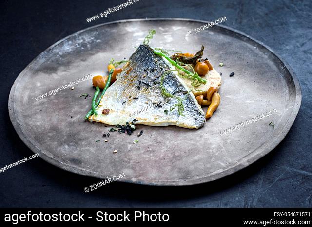 Gourmet fried gilthead fish filet with sliced dumpling, glasswort and algae as closeup on a modern design plate