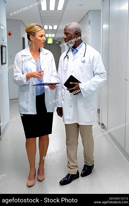 Diverse male and female doctors walking through hospital corridor and talking
