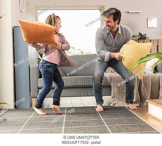 Young man and little girl having a pillow fight in the living room
