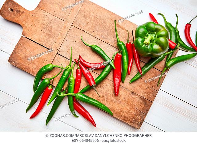Beautiful composition with a wooden old board and colored hot cayenne peppers and green bell pepper on a white wooden background with space under the text