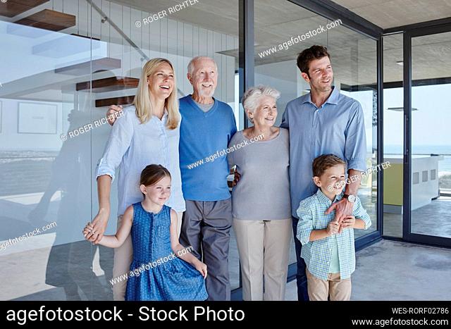 Smiling multi-generation family standing together in front of glass wall looking away