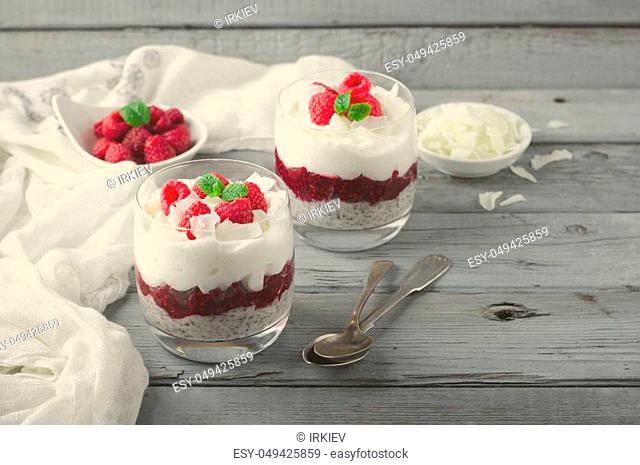 Healthy breakfast, desert, with chia seed pudding, cream, raspberry jam, coconut flakes and fresh berries, on wooden background, toned