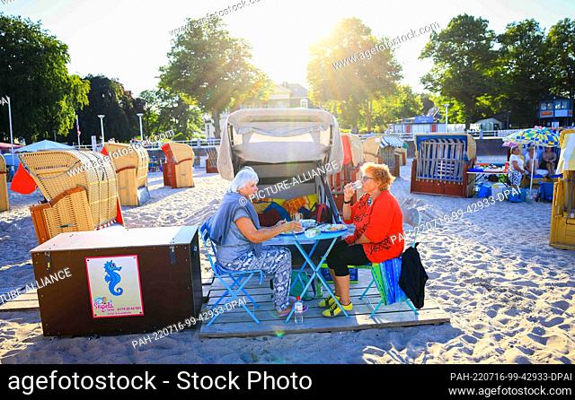 14 July 2022, Schleswig-Holstein, Travemünde: Wiltrud Sadlowski (r) and Marion Schleevoight sit in front of their rented sleeping beach chair on the Baltic Sea...