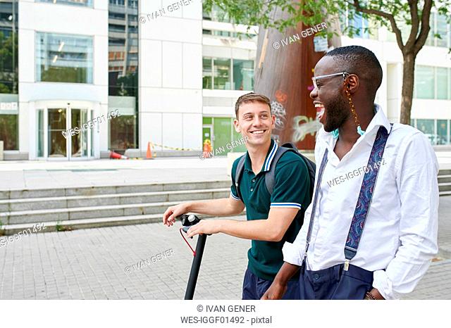 Two happy casual businessmen with e-scooter talking in the city