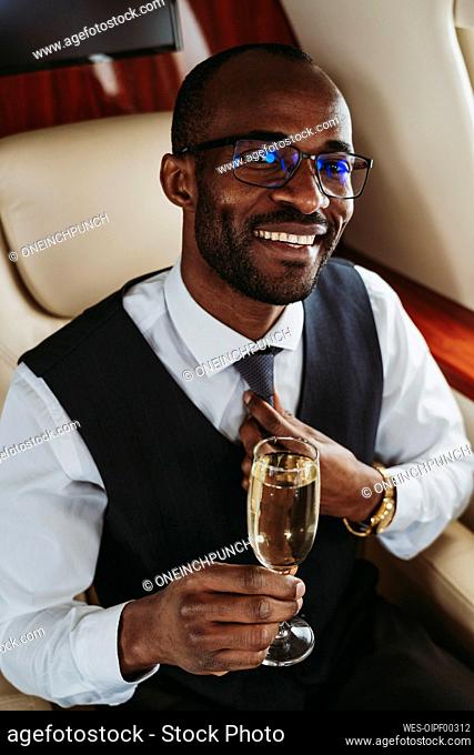 Male entrepreneur with champagne holding necktie while traveling in airplane