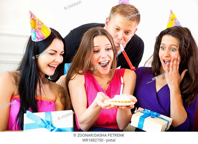 Girl looking at birthday cake surrounded by friends at party