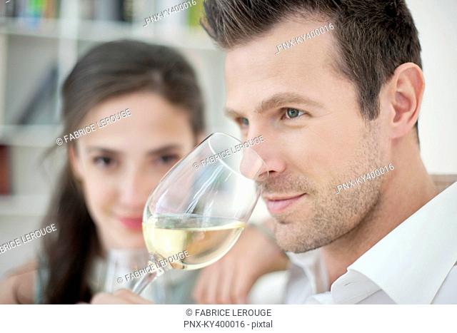 Man drinking white wine with his wife in the background