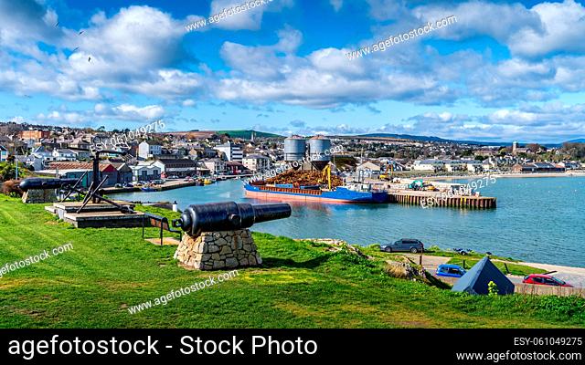 Old naval fortifications and cannons with rusty anchor as landmark and tourist attraction in Wicklow port and village in background, Ireland